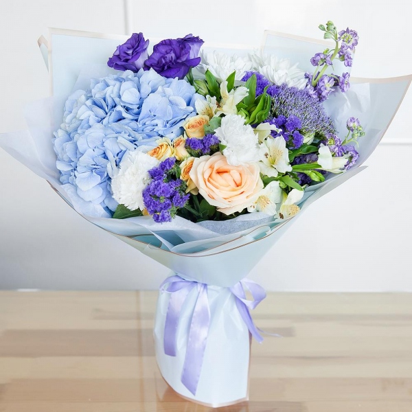 Matthiola Lilac - 2, Rose Cream 50 cm - 1, Carnation white, cream - 2, Spray rose: white, cream, light pink 50 cm - 1, Blue/purple hydrangea - 1, Alstromeria white, soft pink - 2, Baltica White Spray Chrysanthemum - 1, Purple Lisianthus (Eustoma) - 1, Trachelium, Blue Statice, Wrapping Paper